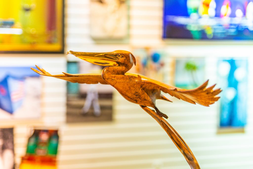 A bird sculpture in front of some paintings.