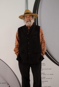 A man in a hat and vest standing next to a wall.