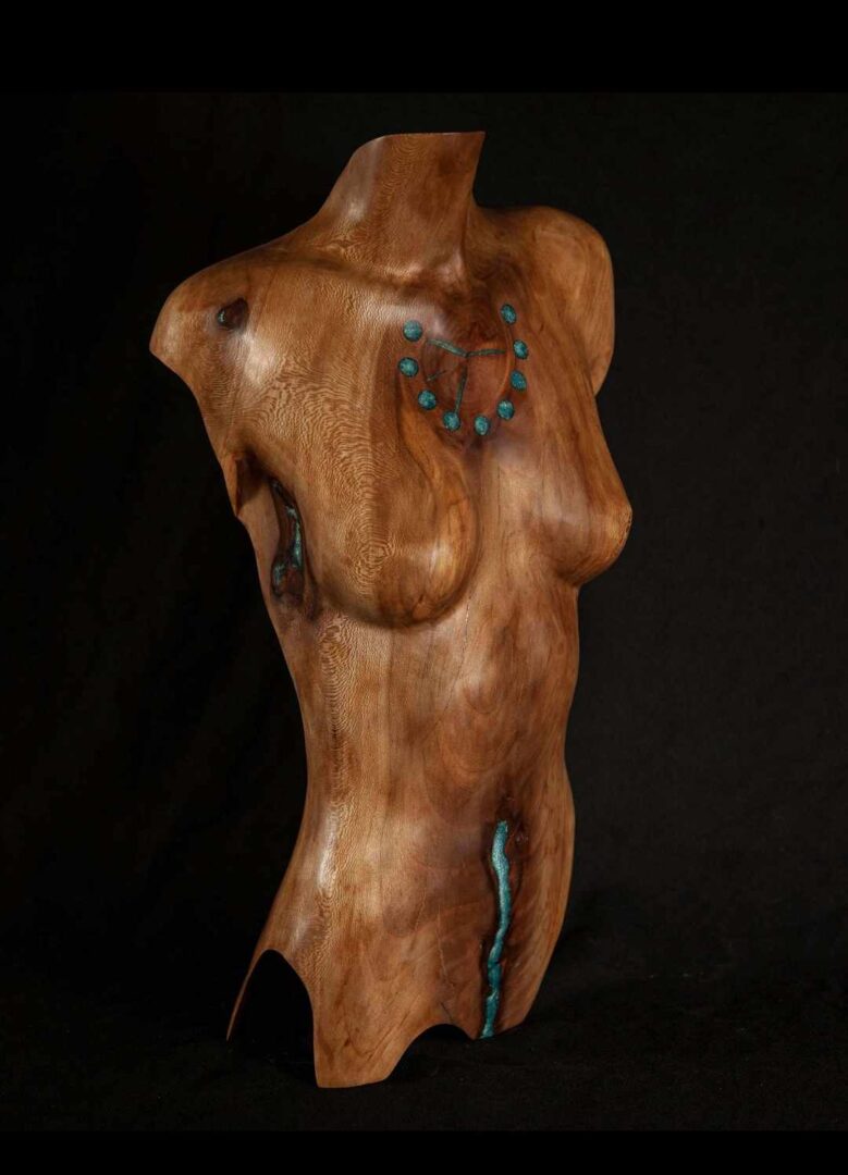 A wooden sculpture of a woman with turquoise jewelry.